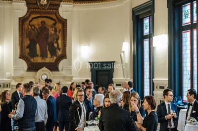 Des personnes discutent en petits groupes lors d'un événement dans une salle élégante avec des vitraux et une fresque murale.