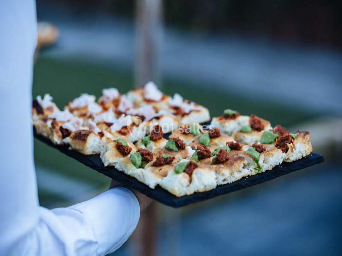 Traiteur Paris (Paris) - Profumo Traiteur Italien #4 Plateau de focaccia garnie de morceaux de viande, herbes fraîches et fromage, tenu par une personne en chemise blanche.