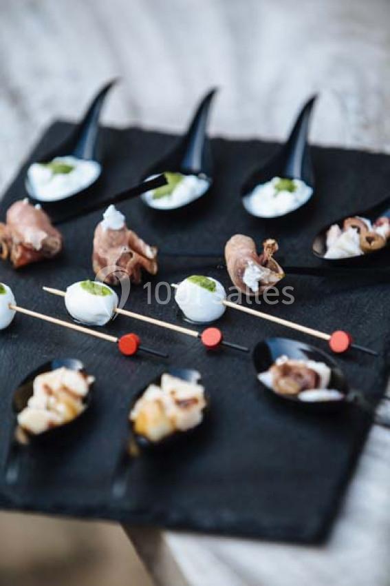 Traiteur Paris (Paris) - Profumo Traiteur Italien #5 Assortiment de bouchées apéritives sur un plateau noir, comprenant brochettes et cuillères garnies.