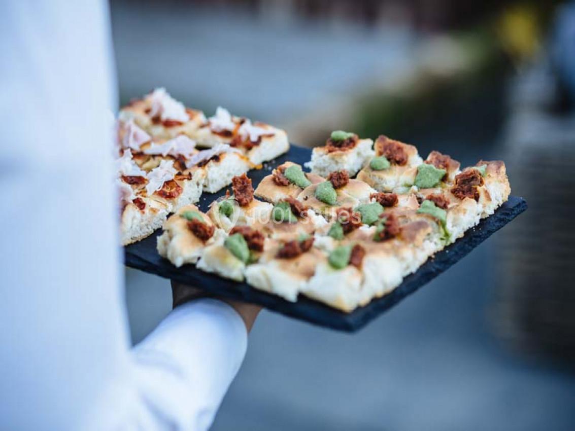 Traiteur Paris (Paris) - Profumo Traiteur Italien #6 Plateau de focaccia garnie de morceaux de viande et d'herbes, tenu par une personne en chemise blanche.
