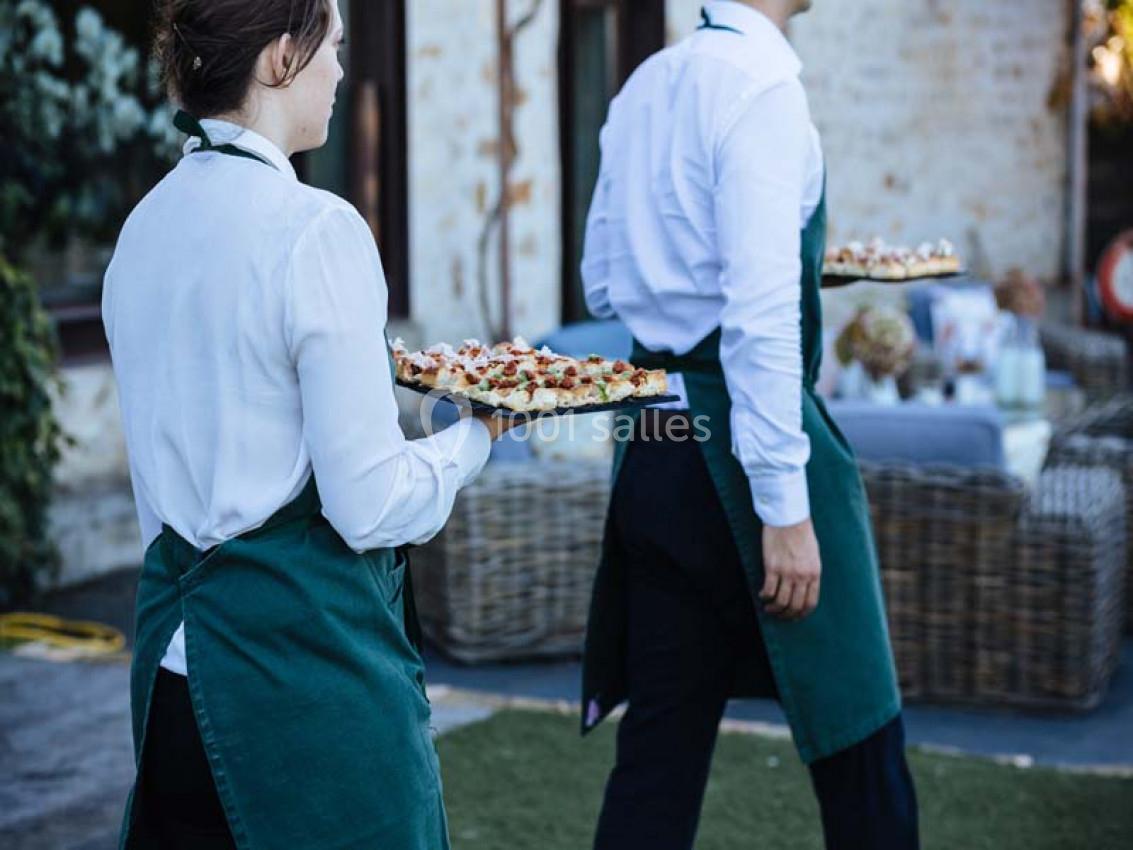 Traiteur Paris (Paris) - Profumo Traiteur Italien #7 Deux serveurs en tablier vert portent des plateaux de nourriture dans un espace extérieur près de tables dressées.
