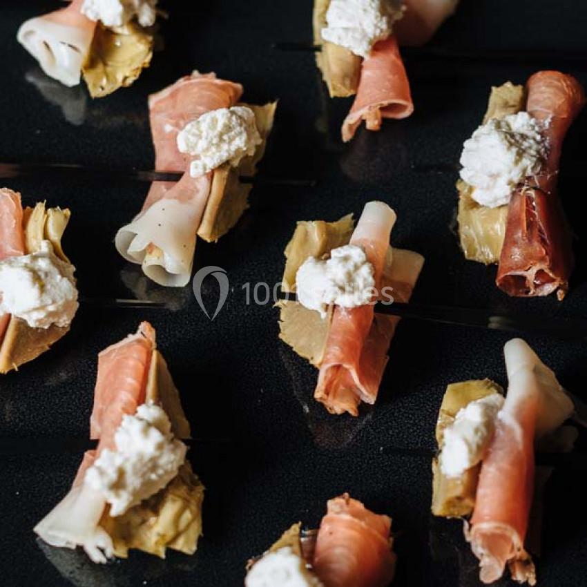 Traiteur Paris (Paris) - Profumo Traiteur Italien #10 Assortiment de bouchées sur des pics, composées de charcuterie, fromage frais et artichauts, disposées sur une surface noire.