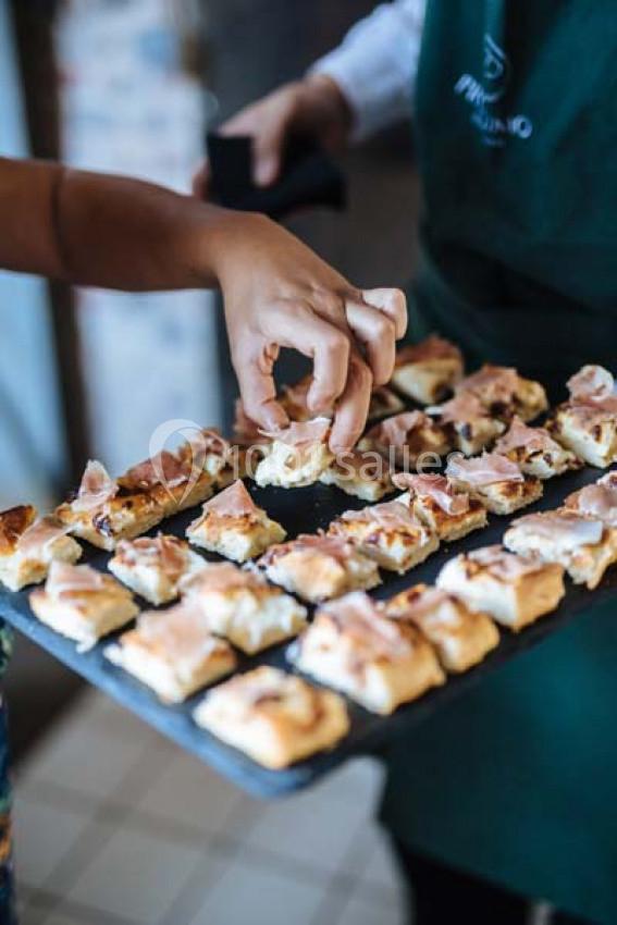 Traiteur Paris (Paris) - Profumo Traiteur Italien #13 Une main prend un morceau de focaccia garnie de jambon sur un plateau tenu par une personne en tablier vert.