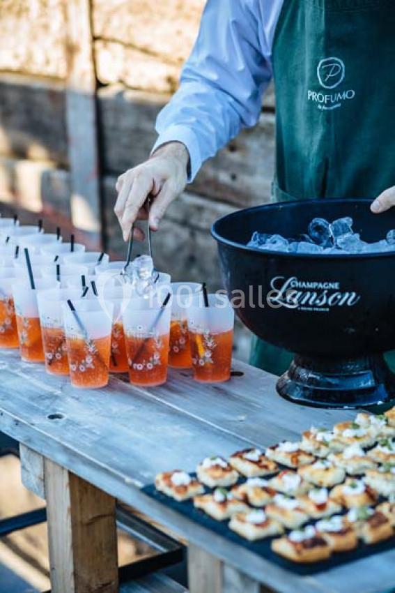 Traiteur Paris (Paris) - Profumo Traiteur Italien #14 Un serveur remplit des verres de cocktail avec des glaçons près d'un plateau de canapés sur une table en bois.