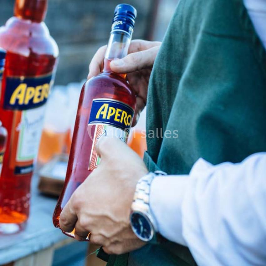 Traiteur Paris (Paris) - Profumo Traiteur Italien #15 Une personne tenant une bouteille d'apéritif rouge avec une étiquette ’Apero’ lors d'un événement en extérieur.