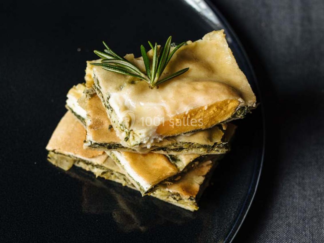 Traiteur Paris (Paris) - Profumo Traiteur Italien #18 Tranches de quiche aux légumes et fromage empilées sur une assiette noire, garnies d'une branche de romarin.