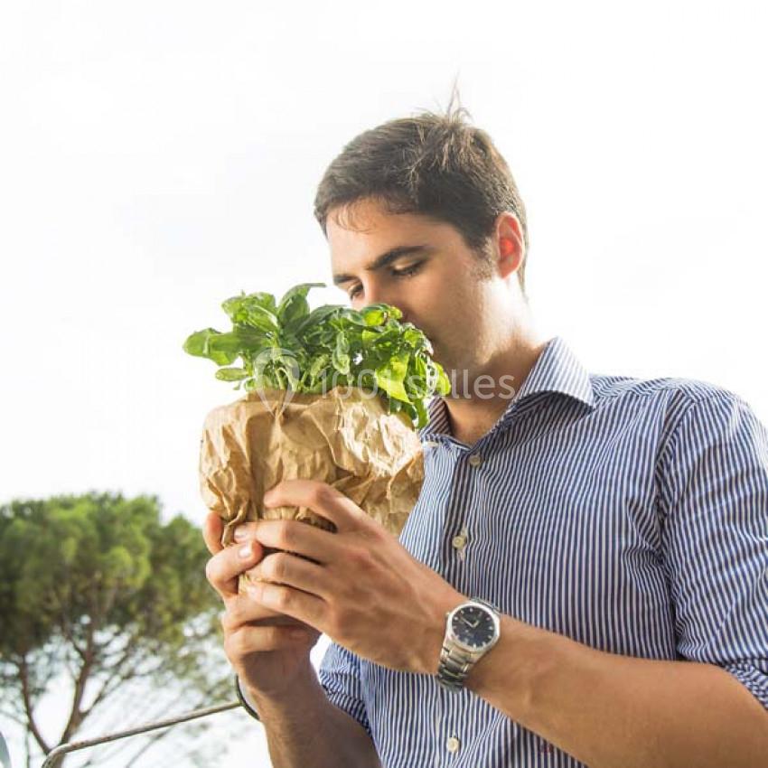 Traiteur Paris (Paris) - Profumo Traiteur Italien #23 Un homme sent un bouquet de feuilles vertes enveloppé dans du papier kraft, en extérieur par temps clair.