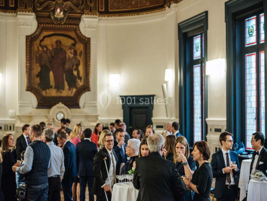 Traiteur Paris (Paris) - Profumo Traiteur Italien #24 Des personnes discutent debout lors d'un événement dans une salle élégante avec des vitraux et une fresque murale.