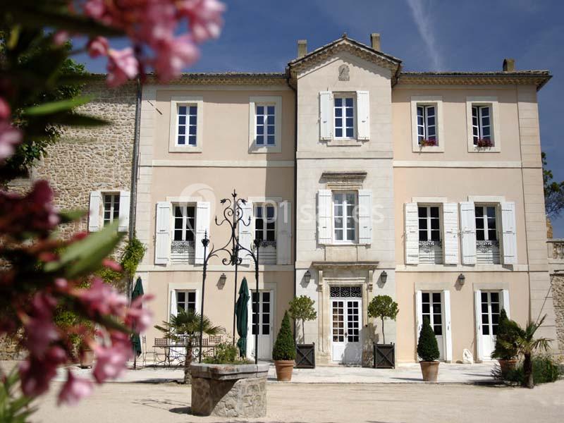 Location salle Sorgues (Vaucluse) - Château La Tour Vaucros #2 Façade d'une maison en pierre à deux étages avec volets blancs, entourée de plantes et d'une cour ensoleillée.