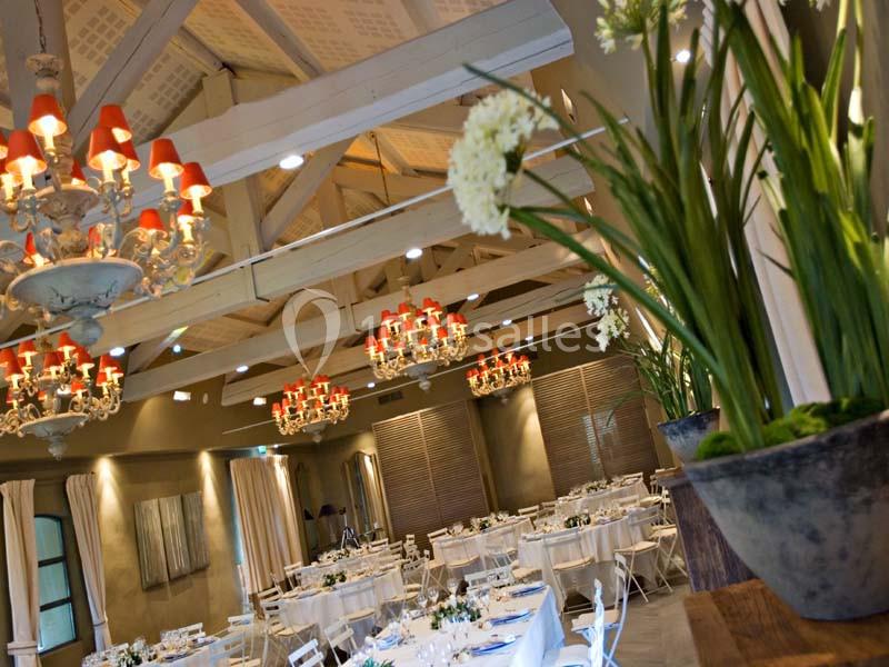 Location salle Sorgues (Vaucluse) - Château La Tour Vaucros #3 Salle de réception élégante avec tables dressées, lustres ornés de lumières rouges et plantes décoratives au premier plan.