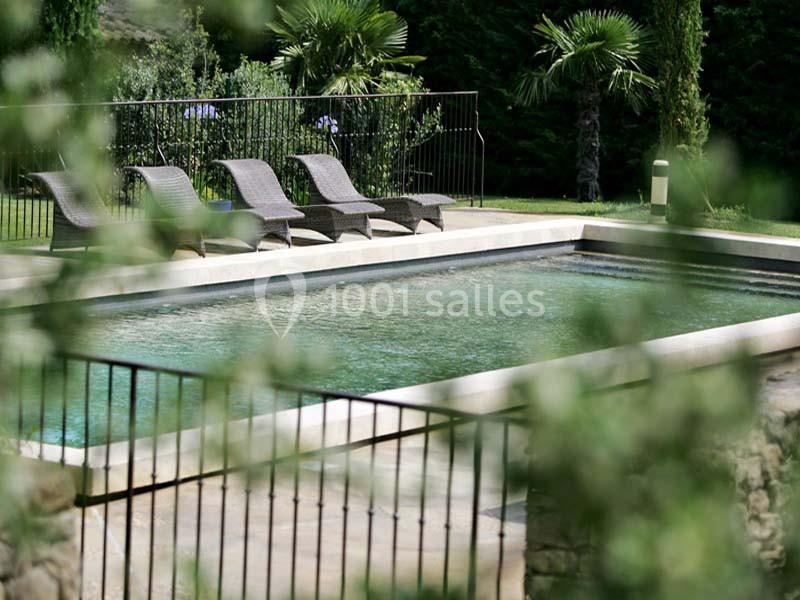 Location salle Sorgues (Vaucluse) - Château La Tour Vaucros #8 Piscine rectangulaire entourée de chaises longues en rotin, bordée de végétation et d'une clôture métallique.