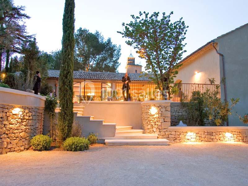 Location salle Sorgues (Vaucluse) - Château La Tour Vaucros #17 Façade d'une maison en pierre avec terrasse éclairée, entourée de végétation et d'arbres au crépuscule.