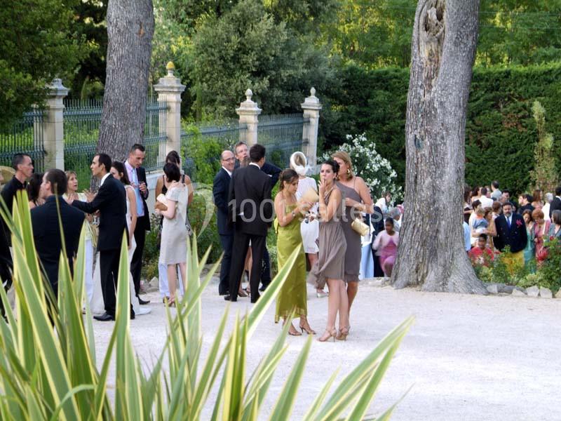 Location salle Sorgues (Vaucluse) - Château La Tour Vaucros #22 Groupe de personnes élégamment vêtues discutant dans un jardin avec des arbres et une allée gravillonnée.