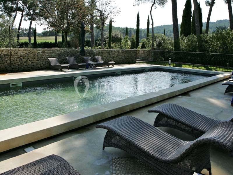 Location salle Sorgues (Vaucluse) - Château La Tour Vaucros #23 Piscine rectangulaire extérieure entourée de chaises longues en rotin, avec vue sur des arbres et un mur en pierre.