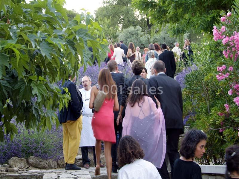 Location salle Sorgues (Vaucluse) - Château La Tour Vaucros #20 Groupe de personnes élégamment vêtues marchant dans un jardin fleuri, entouré de lavandes et d'arbres.