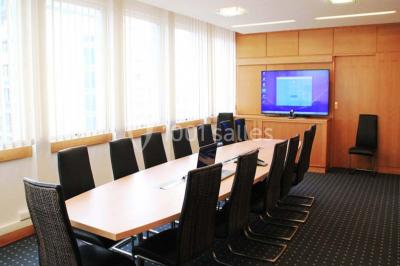 Salle de réunion lumineuse avec table ovale, chaises, paperboard et vue sur la Tour Eiffel à travers de grandes fenêtres.