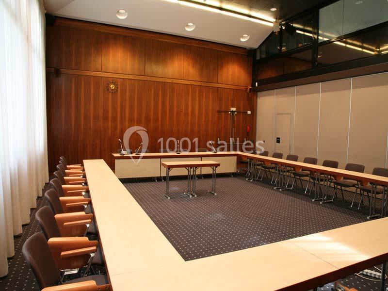 Salle de réunion vide avec tables disposées en U, chaises alignées et murs en bois clair.