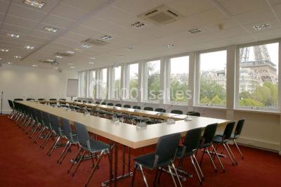 Salle de réunion lumineuse avec table ovale, chaises, paperboard et vue sur la Tour Eiffel à travers de grandes fenêtres.
