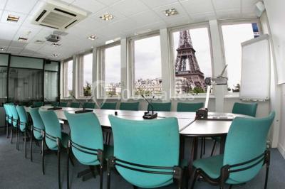 Salle de réunion lumineuse avec table ovale, chaises, paperboard et vue sur la Tour Eiffel à travers de grandes fenêtres.