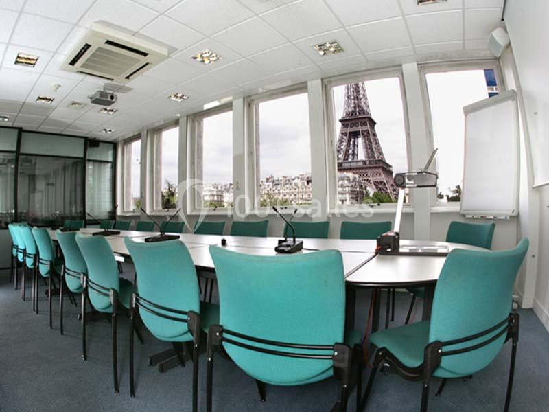 Salle de réunion moderne avec des chaises vertes et vue sur la Tour Eiffel à travers de grandes fenêtres.
