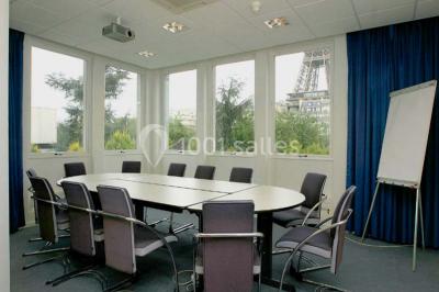 Salle de réunion lumineuse avec table ovale, chaises, paperboard et vue sur la Tour Eiffel à travers de grandes fenêtres.