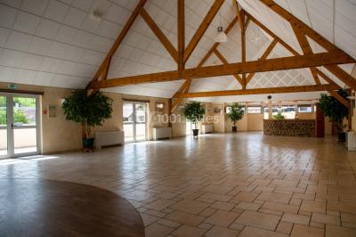 Salle spacieuse avec charpente en bois apparente, carrelage clair et plantes en pots alignées près des fenêtres.
