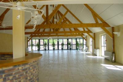 Salle spacieuse avec charpente en bois apparente, carrelage clair et plantes en pots alignées près des fenêtres.