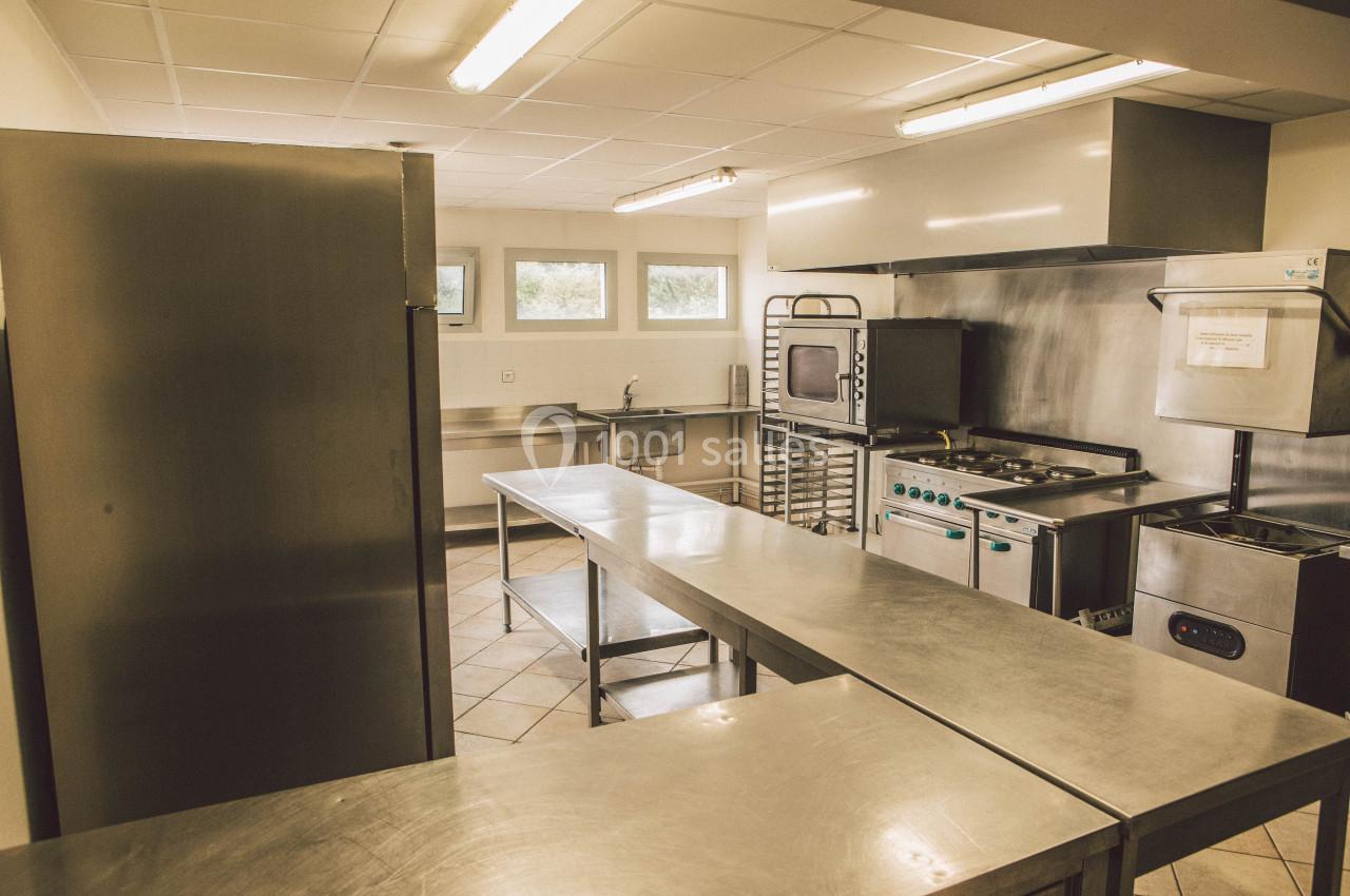 Cuisine professionnelle équipée avec plans de travail en inox, fours, plaques de cuisson et étagères de rangement.