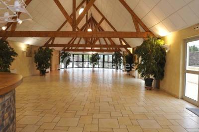 Salle spacieuse avec charpente en bois apparente, carrelage clair et plantes en pots alignées près des fenêtres.