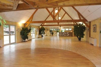 Salle spacieuse avec charpente en bois apparente, carrelage clair et plantes en pots alignées près des fenêtres.
