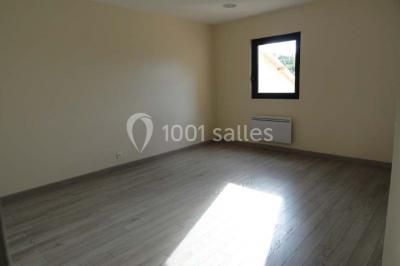 Salle spacieuse avec charpente en bois apparente, carrelage clair et plantes en pots alignées près des fenêtres.