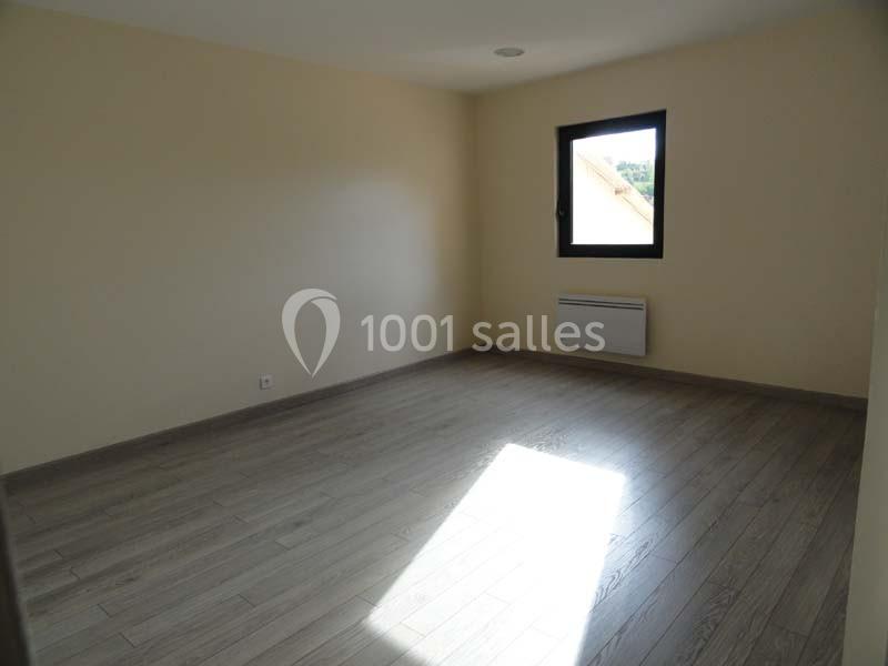 Pièce vide avec murs clairs, sol en parquet et une fenêtre laissant entrer la lumière naturelle.