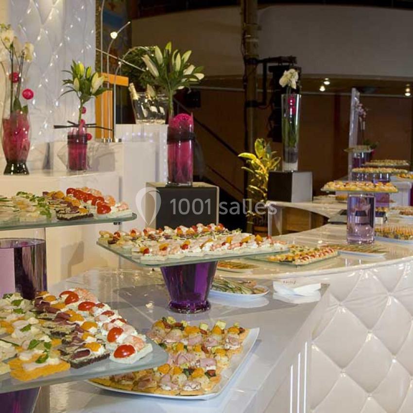 Buffet élégant avec des plateaux de canapés variés, décoré de fleurs et éclairé dans un cadre raffiné.