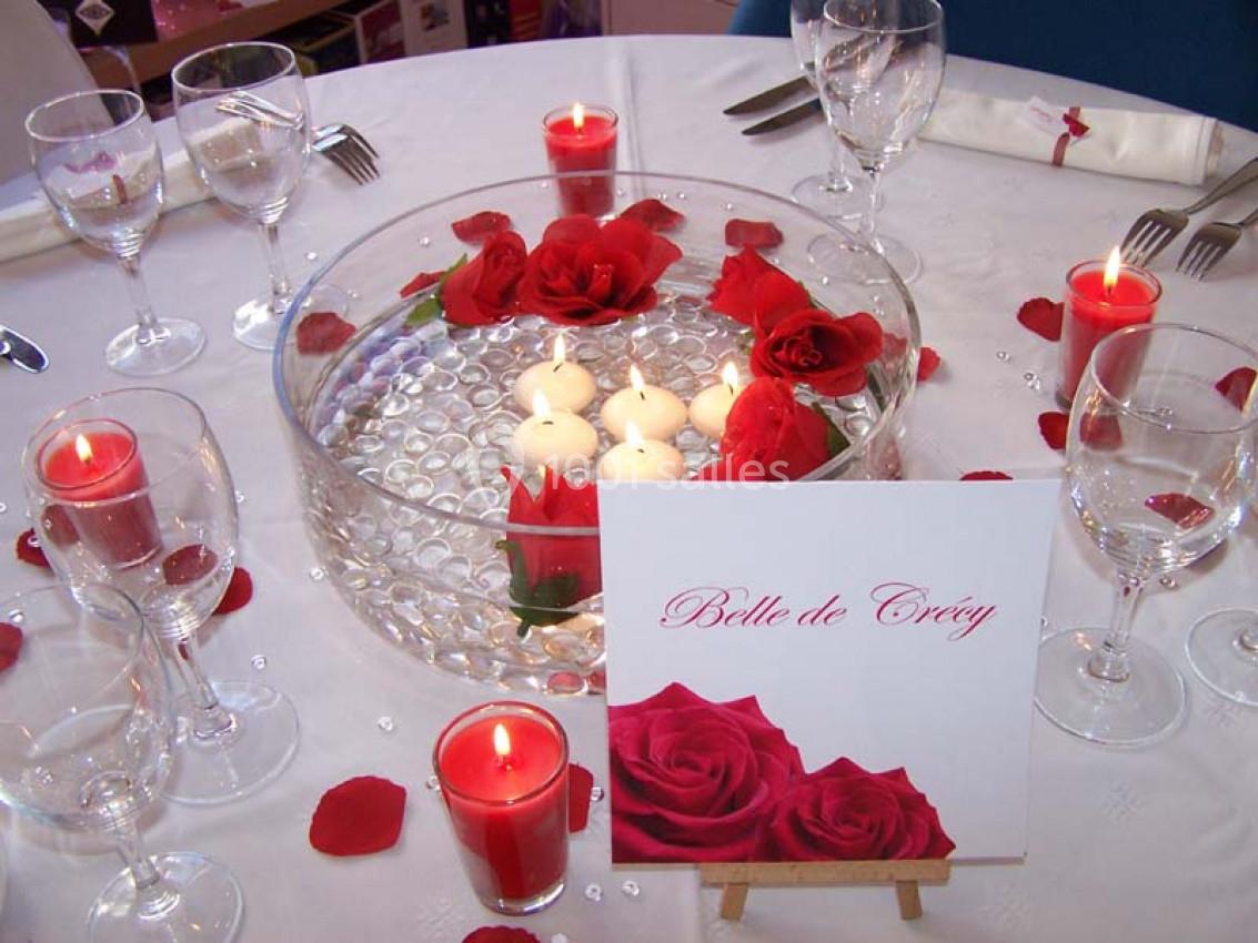 Table décorée avec des bougies flottantes, pétales de roses rouges, verres et une carte avec des roses imprimées.