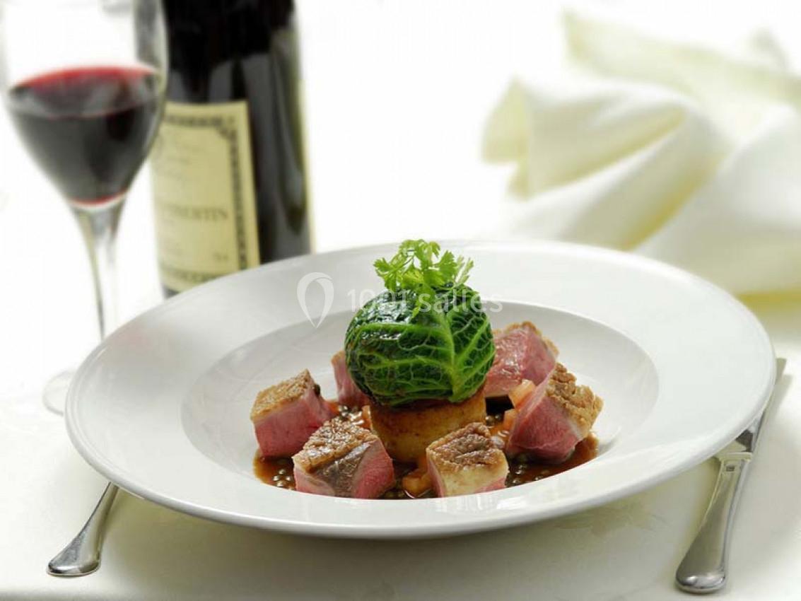 Assiette gastronomique avec viande rosée, chou vert, sauce et garniture, accompagnée d'un verre de vin rouge et d'une…