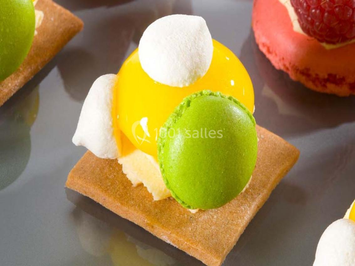 Pâtisserie composée d'une base biscuitée, d'une crème jaune brillante, de meringues blanches et d'un macaron vert.