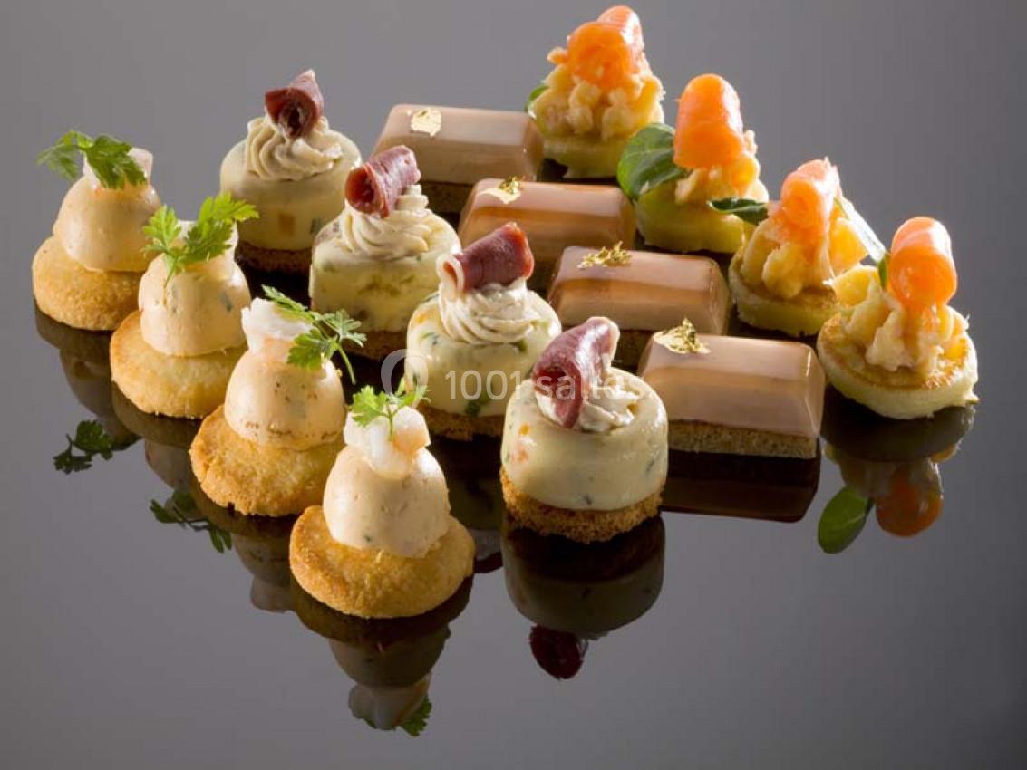 Assortiment de bouchées apéritives raffinées avec saumon, mousse et décorations sur une surface réfléchissante.