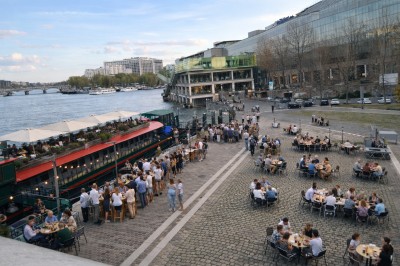 Vue d'un escalier menant à une terrasse animée avec des personnes discutant autour de tables et de plantes.