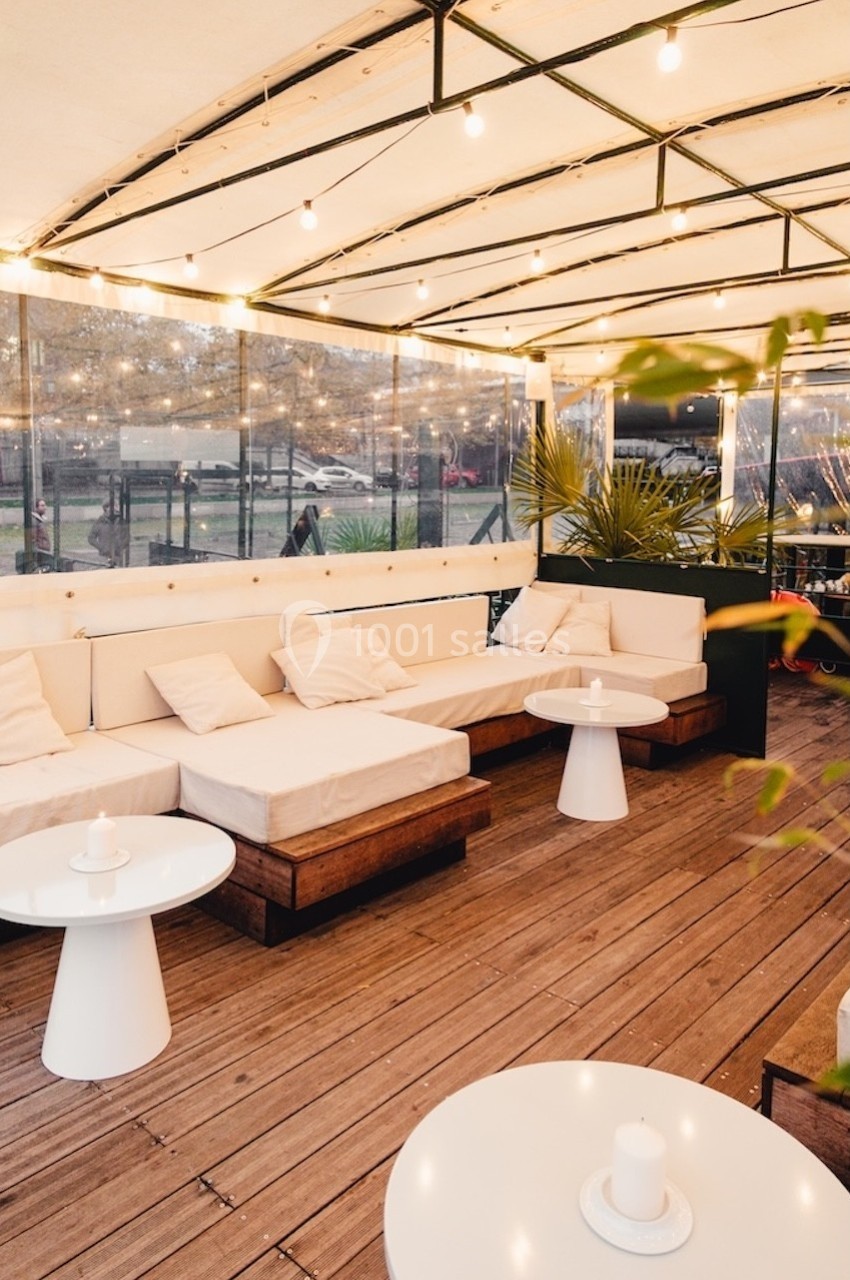 Terrasse couverte avec canapés blancs, tables basses et éclairage suspendu, donnant sur un espace extérieur.