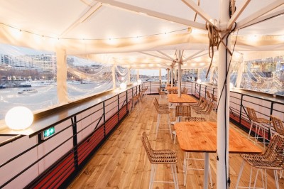 Vue d'un escalier menant à une terrasse animée avec des personnes discutant autour de tables et de plantes.