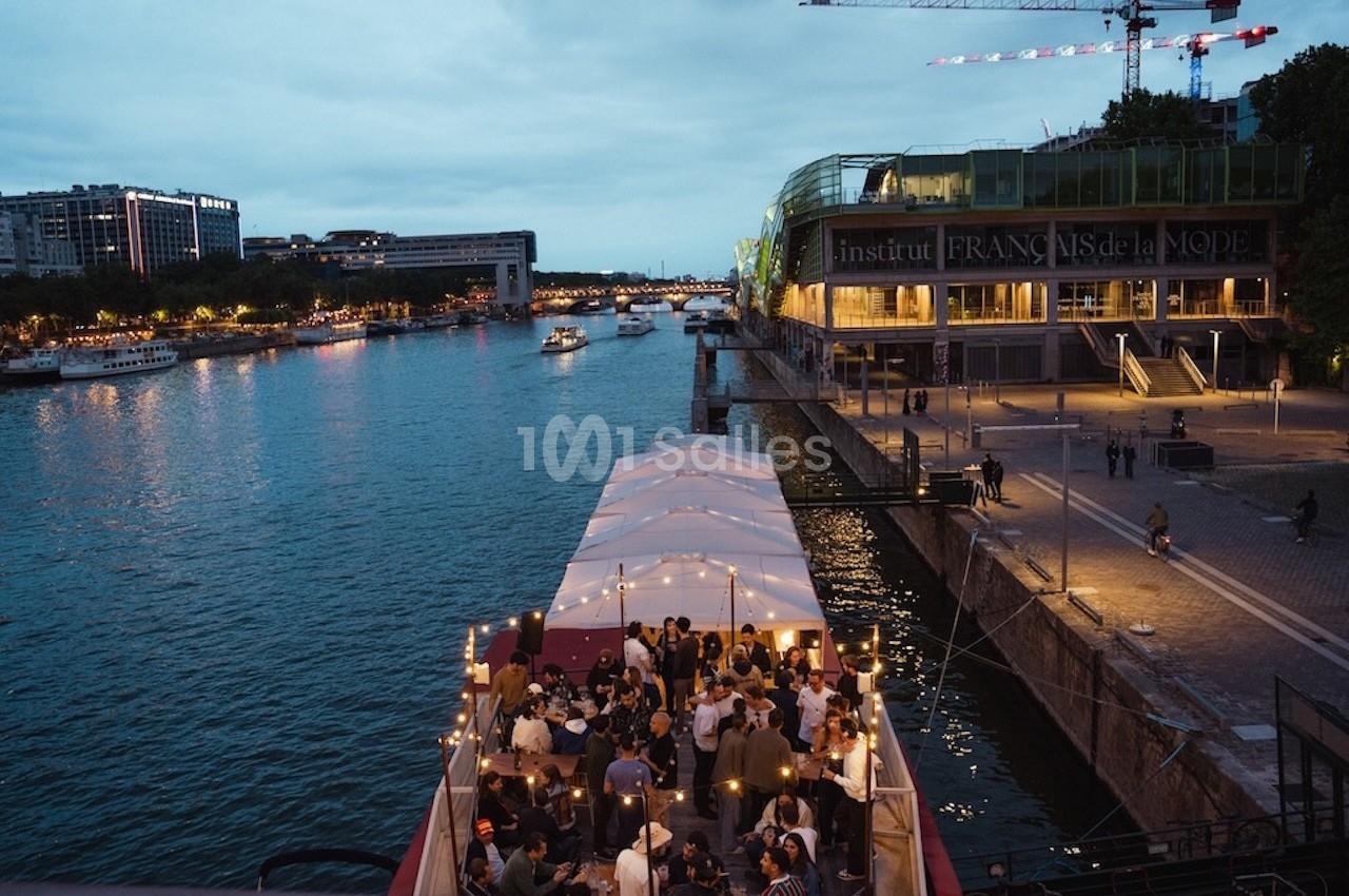 Soirée sur une péniche éclairée, amarrée sur la Seine près de l'Institut Français de la Mode au crépuscule.