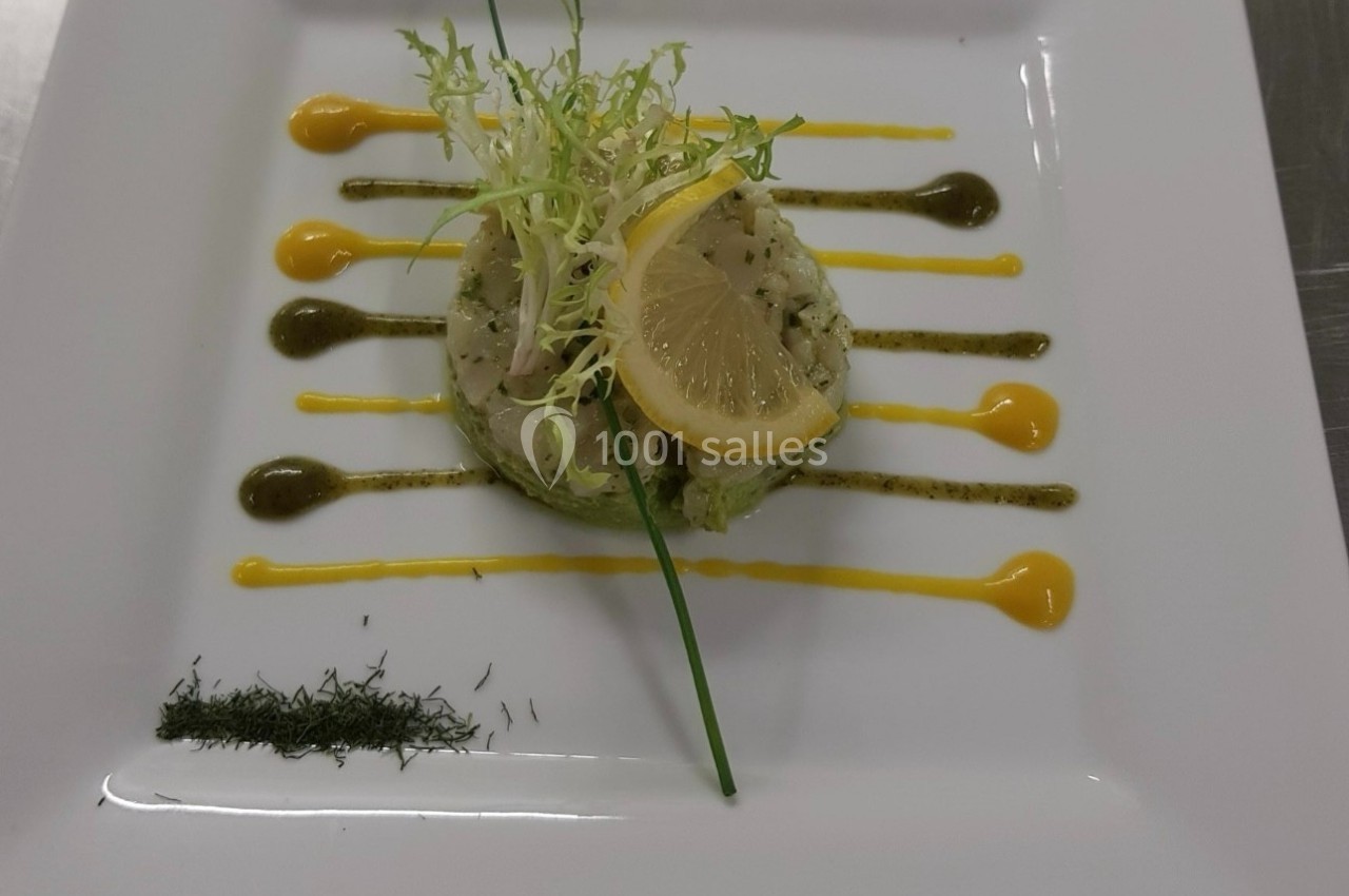 Assiette de tartare de poisson décorée de sauces colorées, d'herbes fraîches, d'une tranche de citron et de salade.