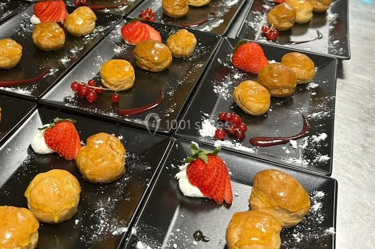 Assiettes noires garnies de choux dorés, fraises, groseilles, crème et filet de coulis rouge.