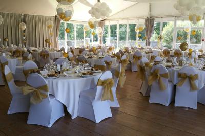Salle de réception décorée avec des tables rondes et rectangulaires, nappes blanches, chaises blanches et guirlandes…