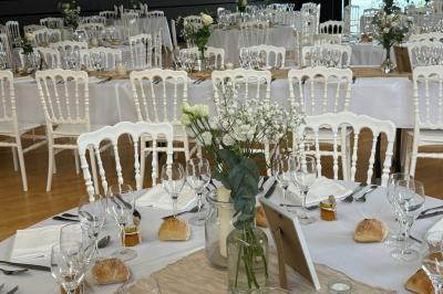 Salle de réception décorée avec des tables rondes et rectangulaires, nappes blanches, chaises blanches et guirlandes…