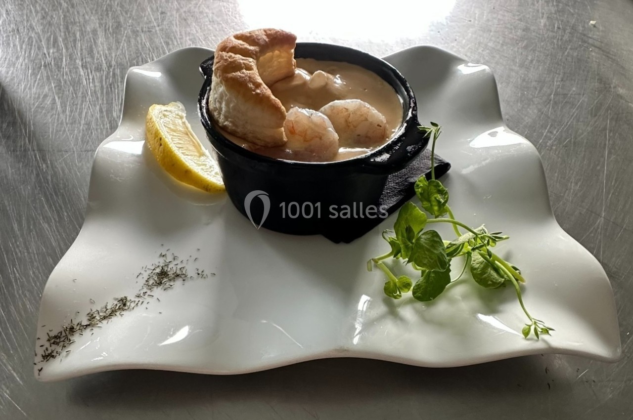 Plat de fruits de mer en sauce dans une cassolette noire, accompagné d'une tranche de citron et d'herbes fraîches.