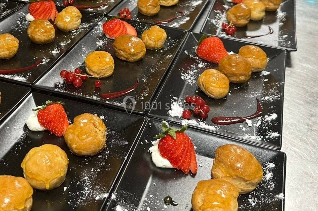 Assortiment de desserts avec choux glacés, fraises, groseilles et crème, présentés sur des assiettes noires.