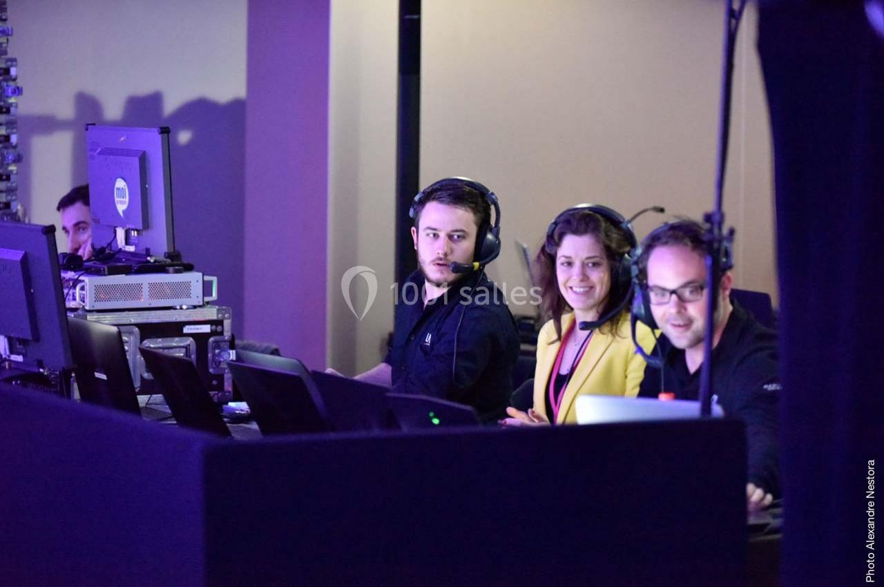 Des techniciens et une femme souriante travaillent sur des ordinateurs et équipements audio dans une régie technique.