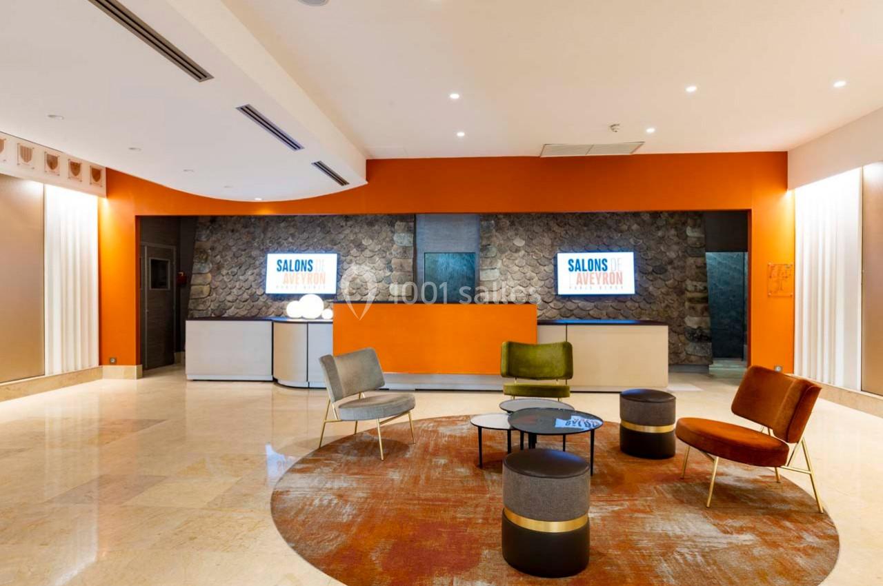 Espace d'accueil moderne avec comptoir orange, sièges colorés, tables basses et écrans affichant ’Salons Avignon’.