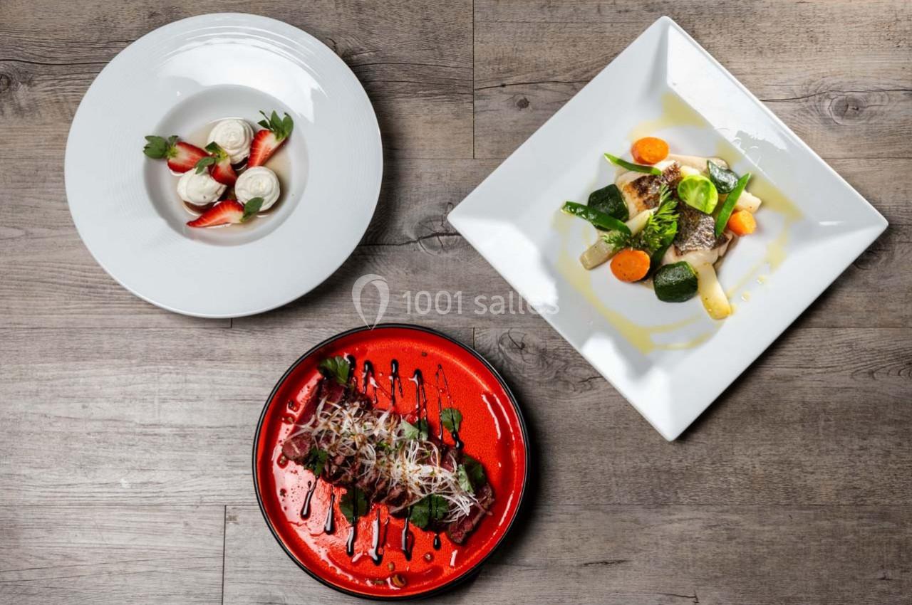 Trois assiettes de plats gastronomiques variés présentées sur une table en bois.